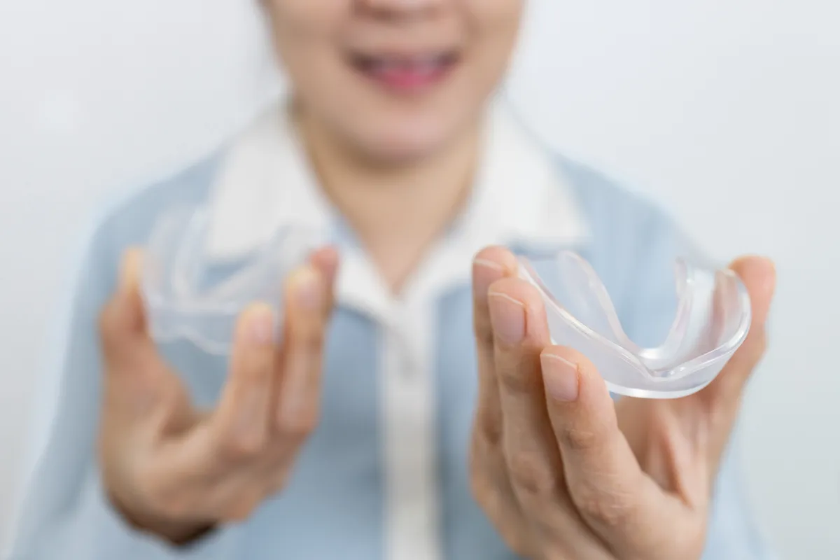 Mulher segurando duas moldeiras para clareamento dental com as mãos — dispositivos transparentes utilizados para aplicar gel clareador e promover o branqueamento dos dentes em casa.